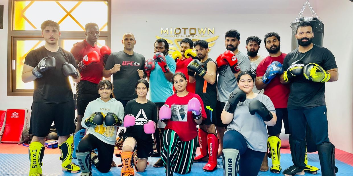 Kickboxing group in front of the Midtown Martial Arts Club wall logo, Jaddaf